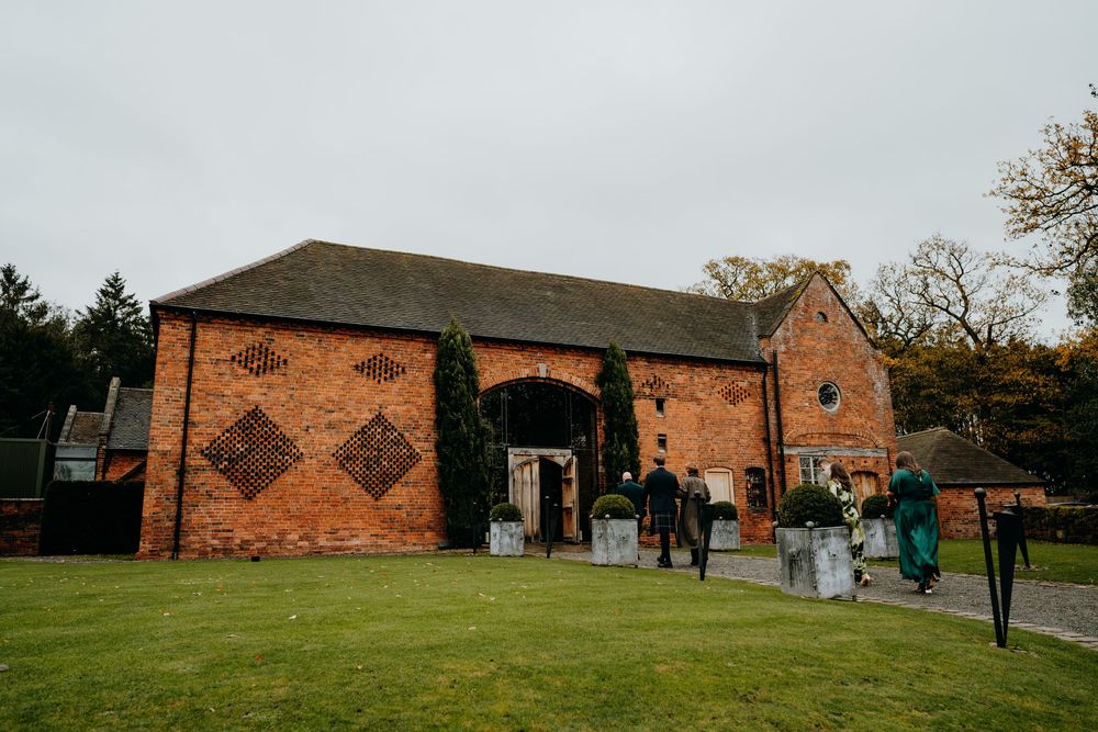 Rustic red brick barn wedding venue exterior with guests arriving on an overcast autumn day.
