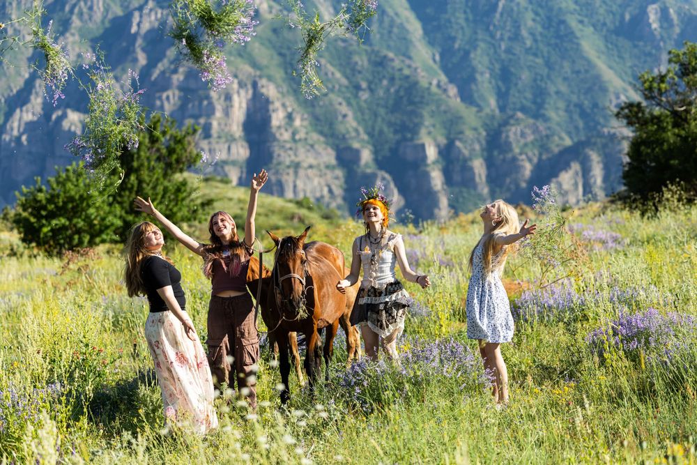 Four women celebrating with a horse in a lush green mountain meadow filled with wildflowers.