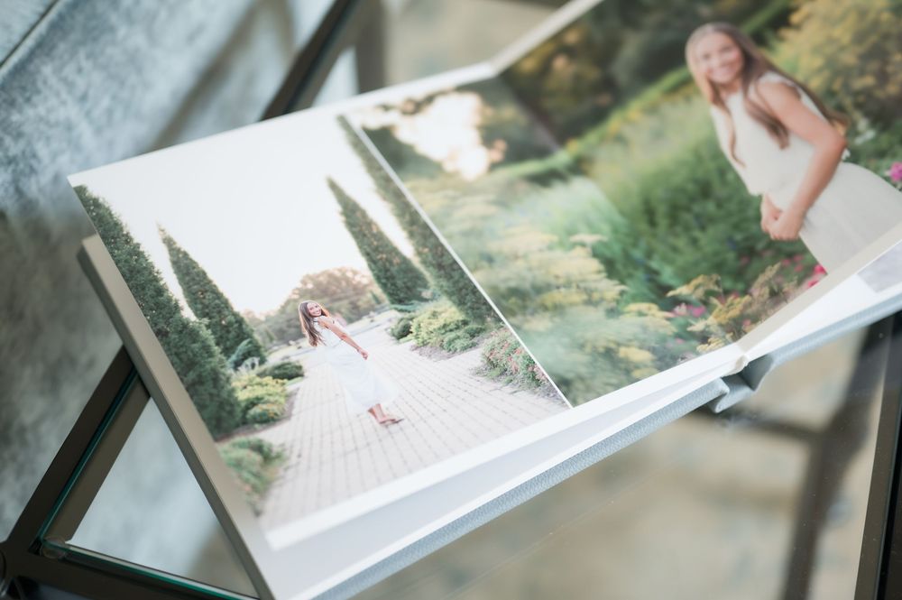 Open photo album on a stand showing portrait pages of a woman in a white dress walking through a landscaped garden path.