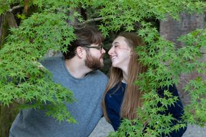 Happy couple sharing a romantic moment surrounded by lush green Japanese maple tree branches outdoors.