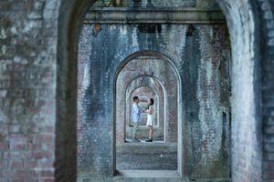 Two people stand within a series of receding brick archways creating a dramatic tunnel perspective at a historic structure.