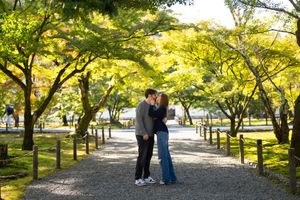 Couple sharing a romantic kiss on a tree-lined gravel path in a lush Japanese garden during autumn.