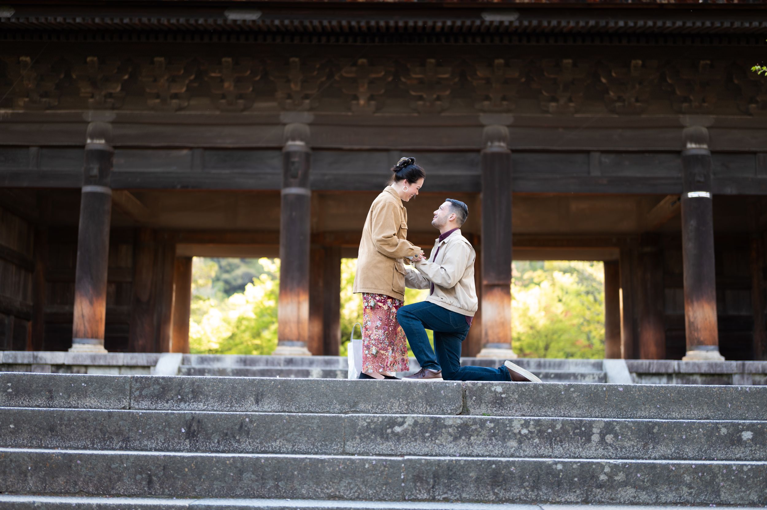 Man proposing to woman on temple steps in Japan, both in traditional attire, romantic outdoor setting.