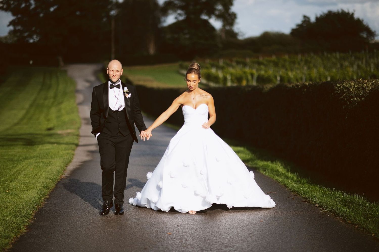 Bride and groom walking hand in hand along a sunny path beside the vineyard at Sandhole Oak Barn