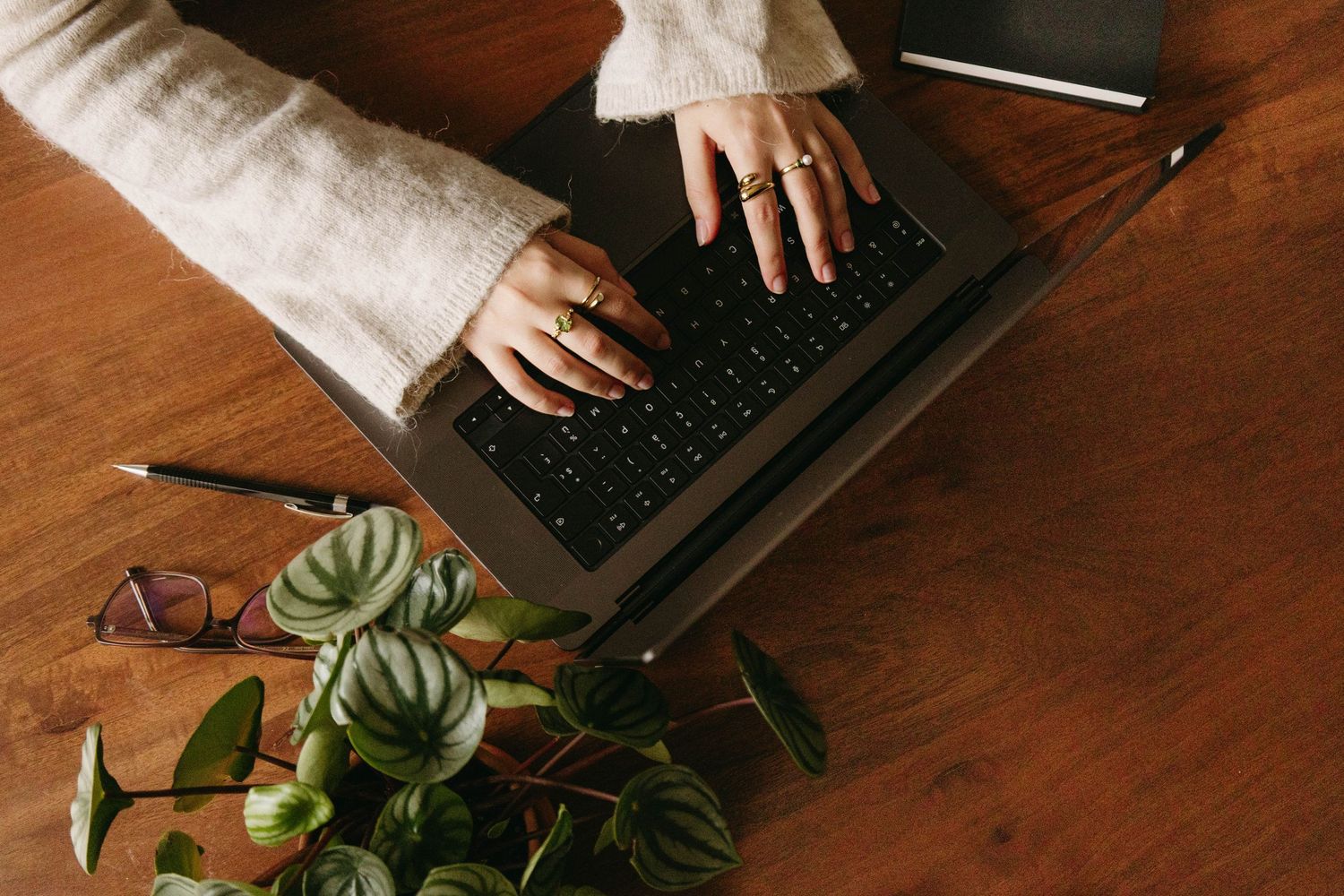 Overhead view of woman's hands with rings typing on laptop on wooden desk.