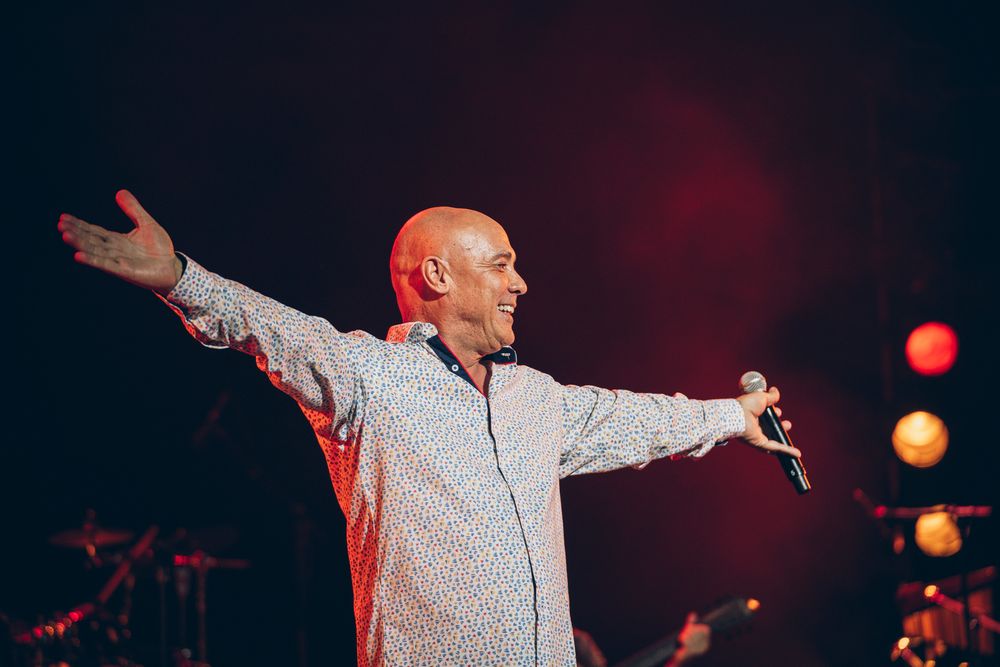 Performer with arms spread wide on stage with red lighting effects.
