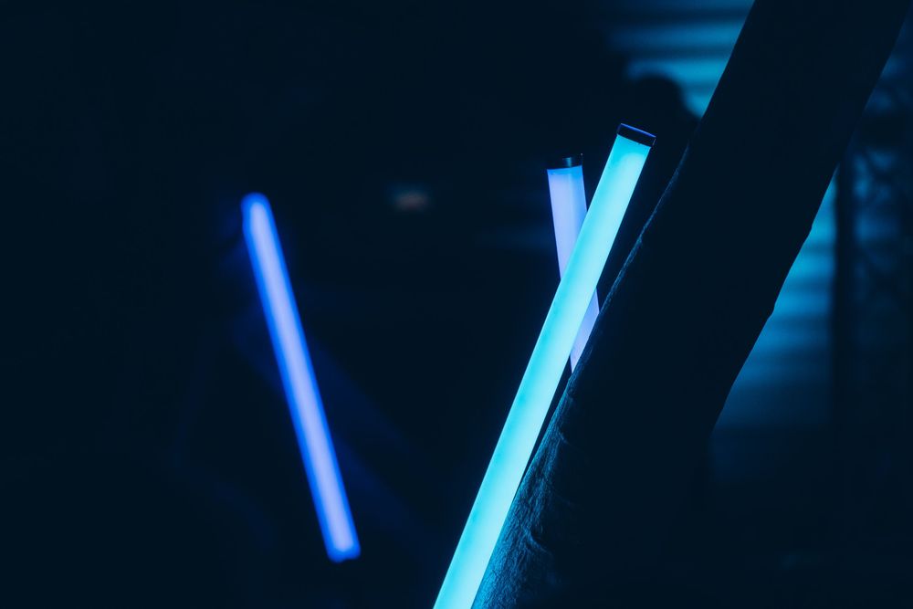 Two glowing blue neon light tubes in a dark room creating a dramatic cyan illumination effect.