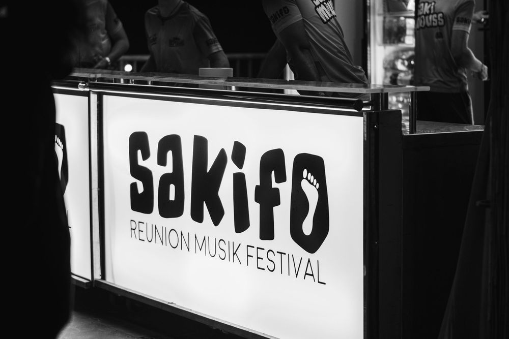 Black and white photo of Sakifo Reunion Musik Festival branded display booth sign at an outdoor event.