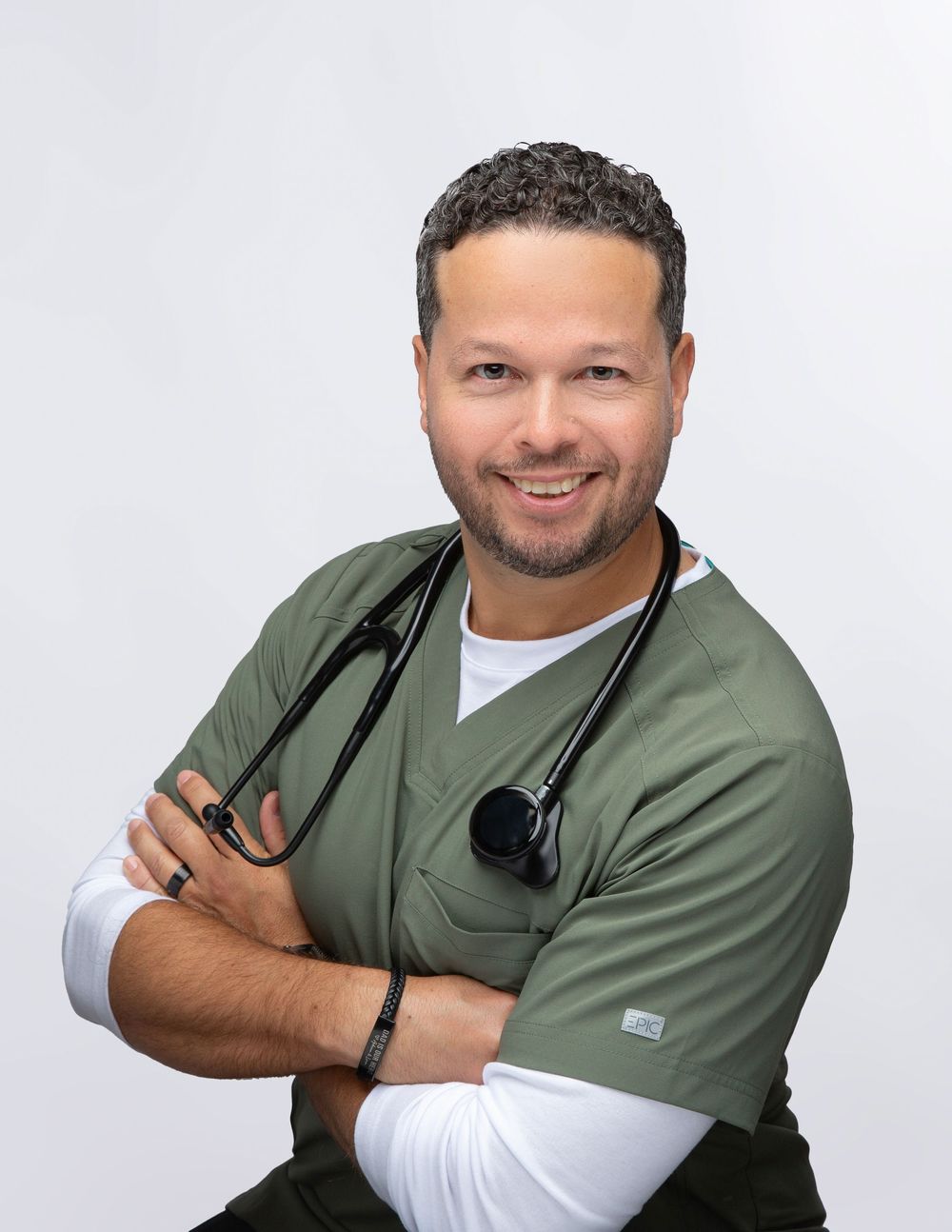 Man in an olive top with a stethoscope on a white backdrop, business casual headshot