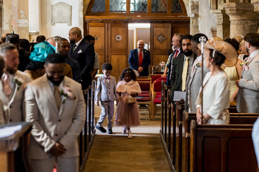Children walk down a church aisle during a wedding ceremony, with guests seated in wooden pews.