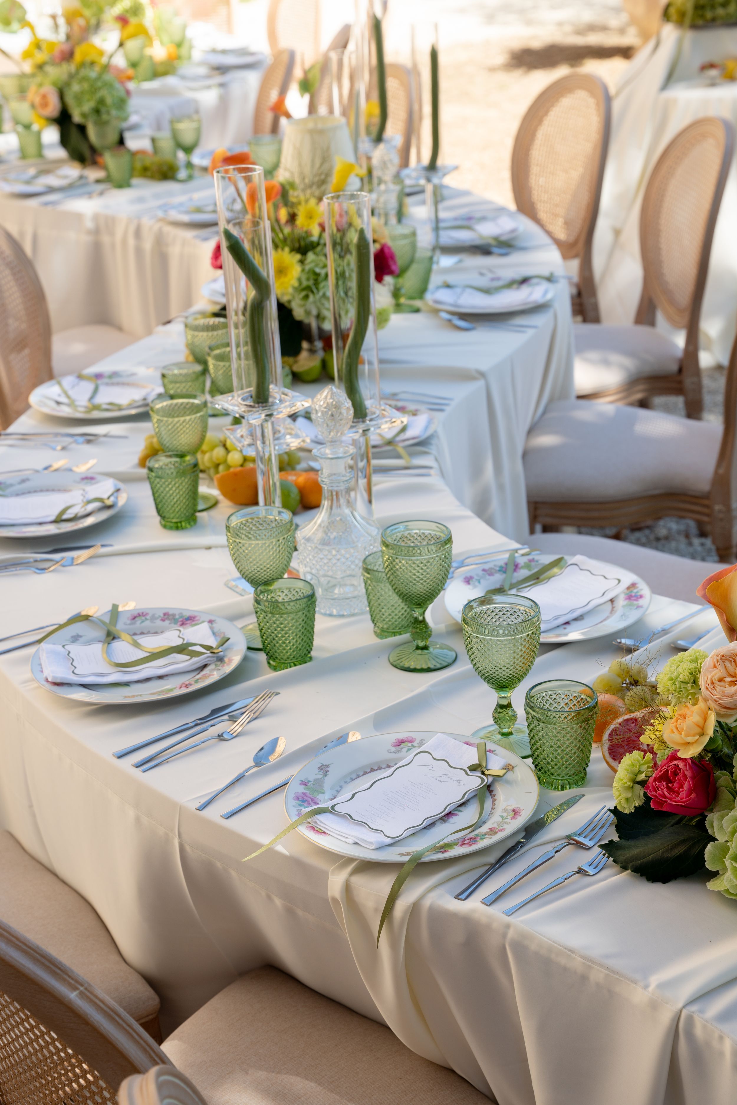 Elegant outdoor wedding table setting with green glassware, floral centerpieces, white linens, and fine china place settings.