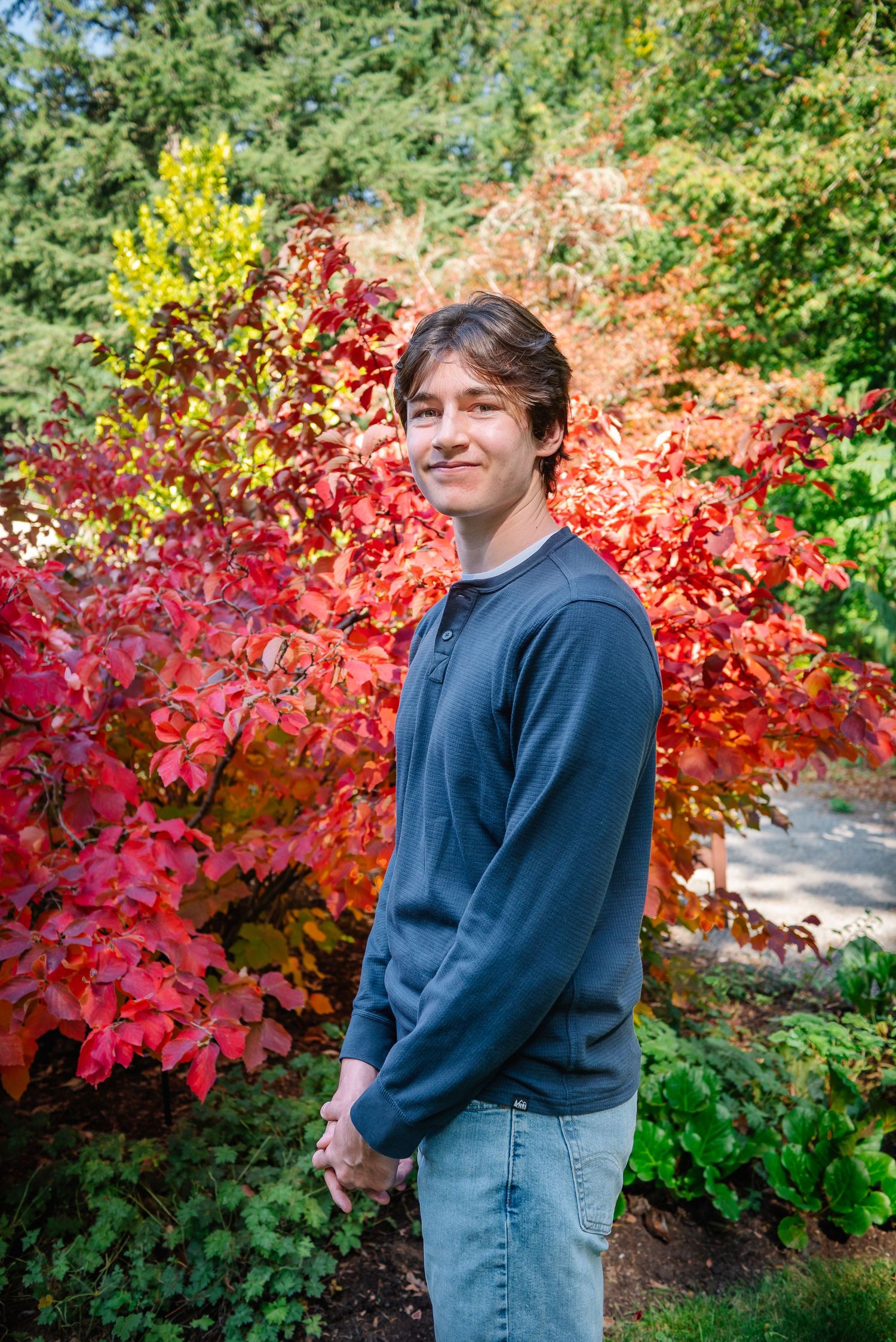 High school senior in a green shirt posing in front of vivid red autumn leaves