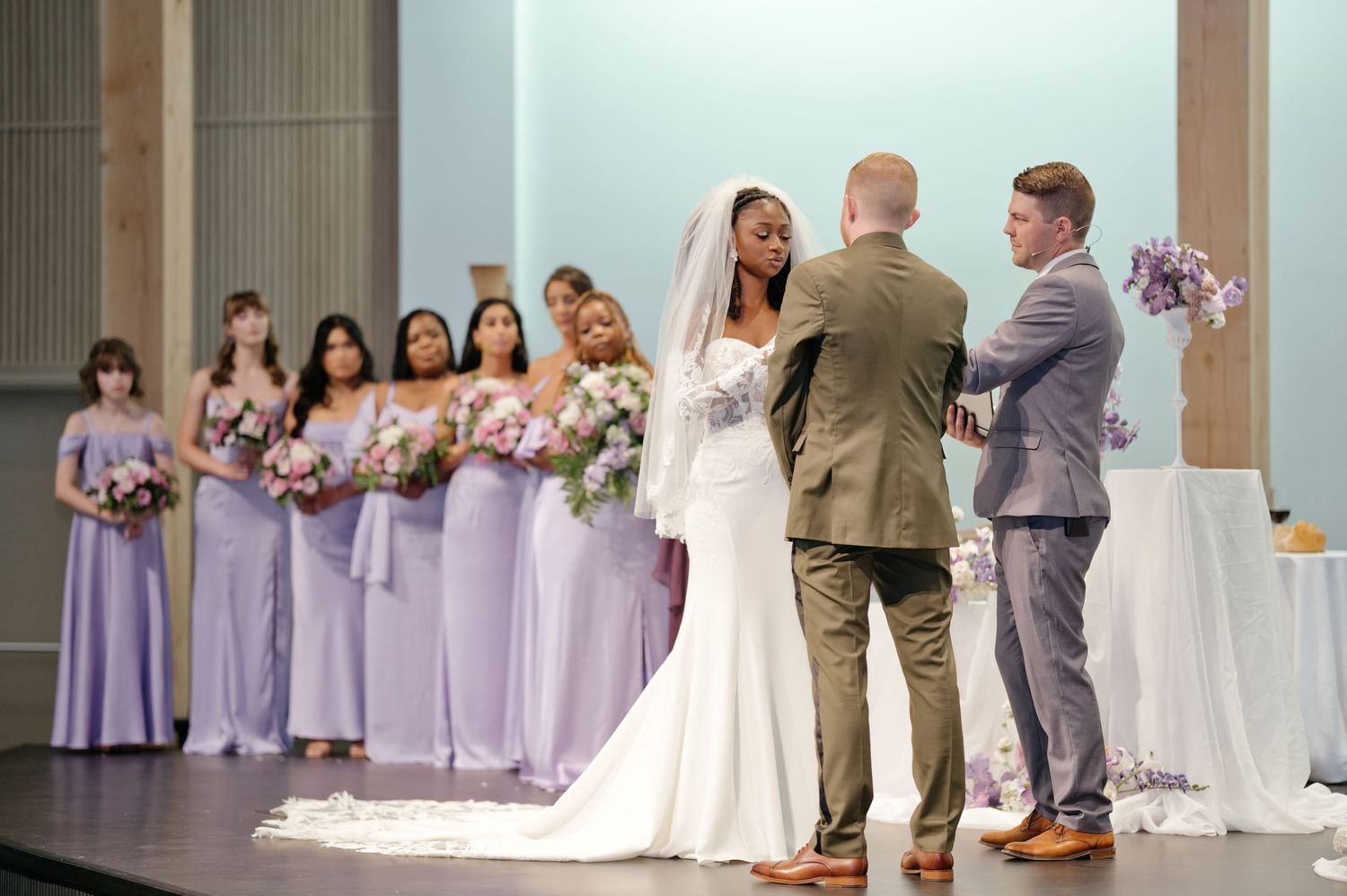 Karen in a white gown and veil stands at the church altar with Yan, while bridesmaids in lavender dresses hold bouquets nearby.