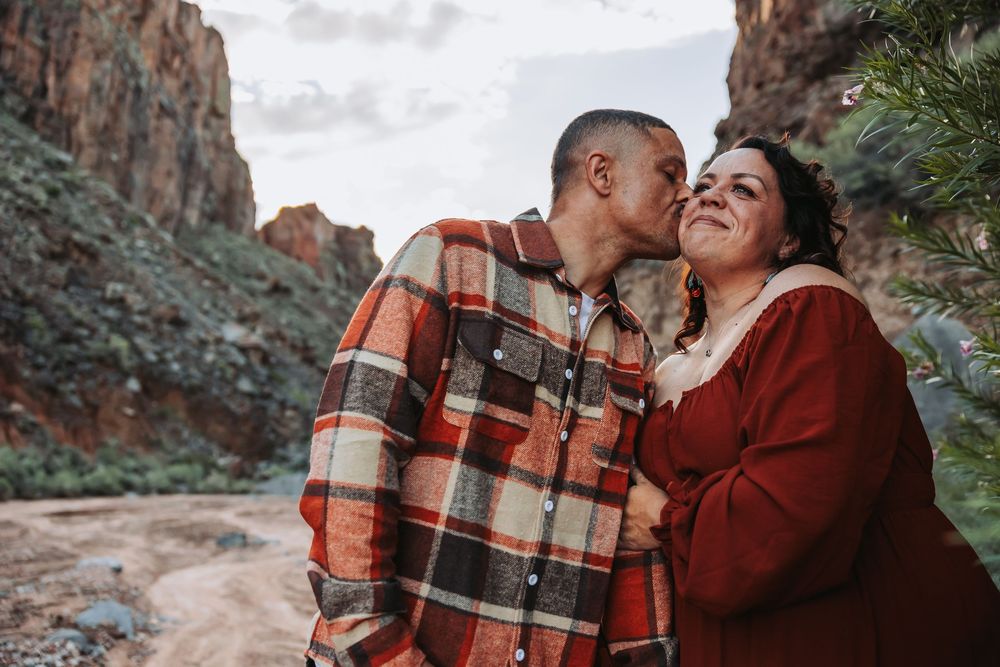 Couple sharing a romantic kiss in a red rock canyon, wearing cozy flannel shirts in autumn tones.