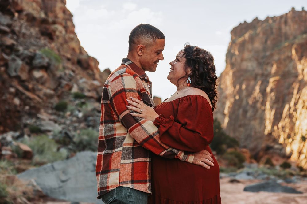Couple embracing and gazing at each other in a rocky canyon, wearing plaid and red outfits during golden hour.