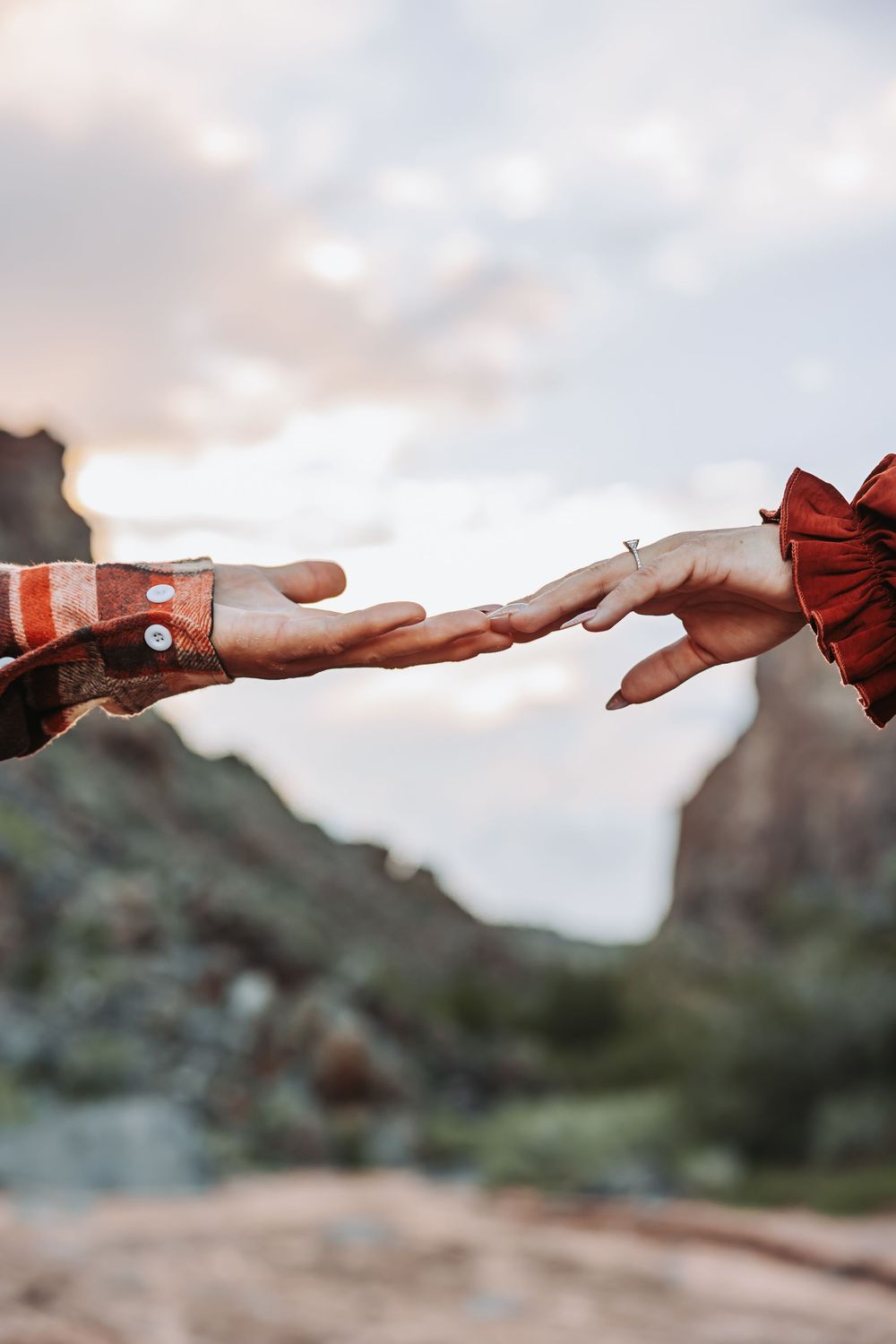Two hands reaching toward each other against a scenic mountain backdrop, evoking romance and connection outdoors.