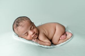 Sleeping newborn baby curled up in a cozy side-lying pose on a soft pale green blanket during a professional newborn photoshoot.