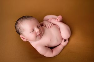 Sleeping newborn baby curled up on a warm golden-brown backdrop in a peaceful newborn photography session.