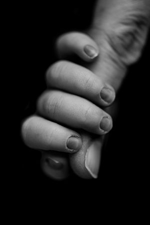 Black and white close-up of a hand with curled fingers and short, bitten nails against a dark background.
