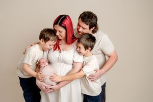 Family newborn portrait of a red-haired mother holding her baby, with a father and two young boys gathered close in white outfits.