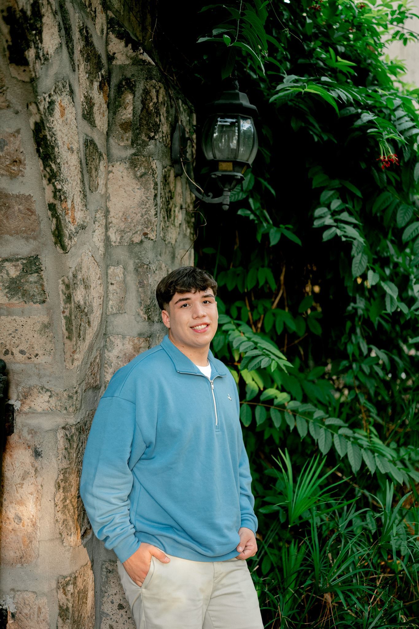 High school senior guy leaning against stone column.