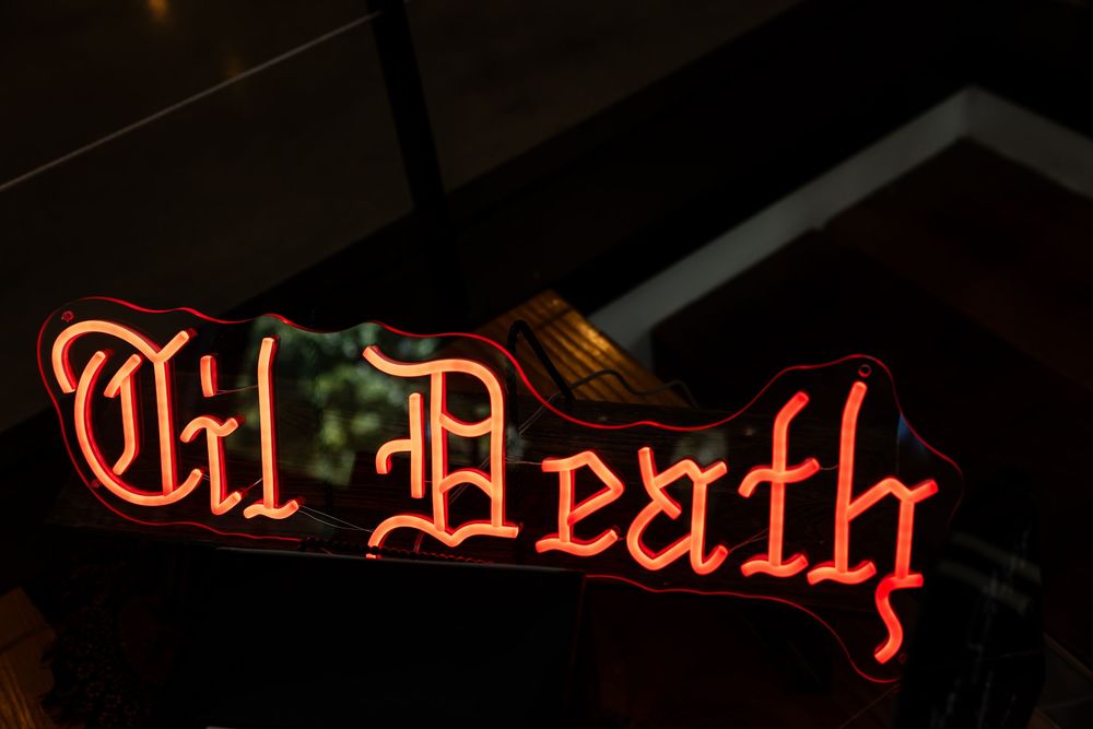 Red neon sign in gothic blackletter script reading "Til Death" glowing against a dark background.