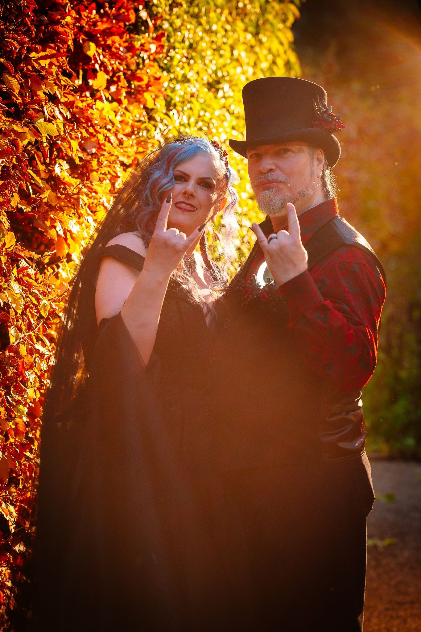 Bride and groom in a top hat making devil horns against glowing orange autumn leaves at Le Petit Chateau