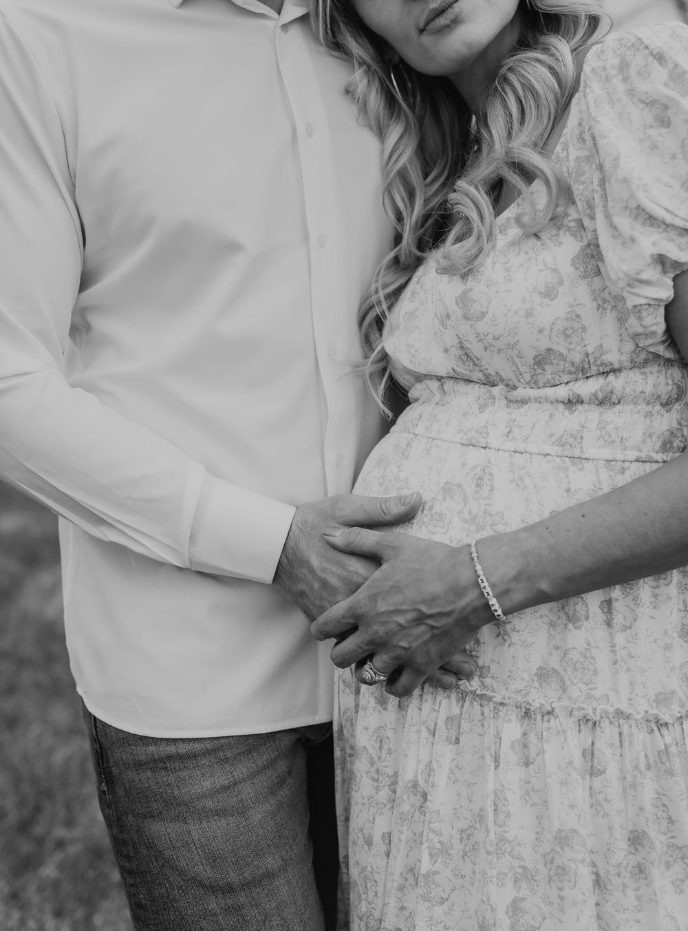 Black and white close-up of couple holding pregnant belly outdoors.