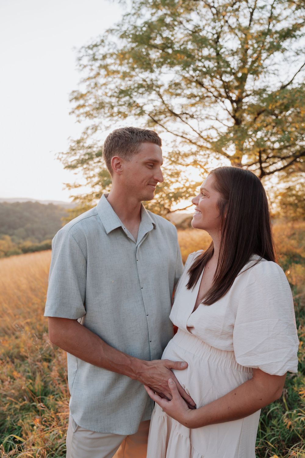 Expecting couple gazing at each other lovingly in golden field during outdoor maternity photography session.