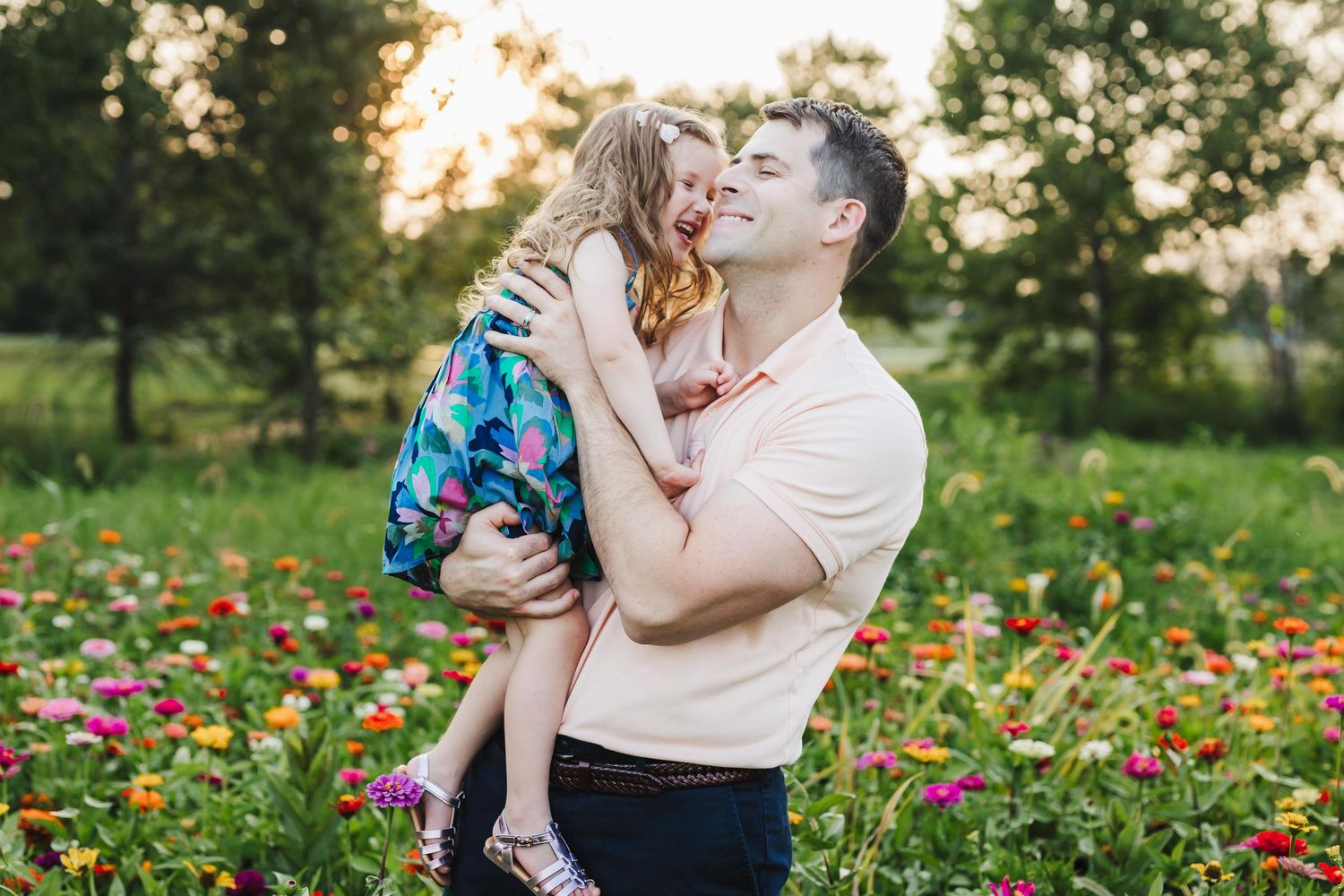 A father joyfully lifts his young daughter in a vibrant flower field at golden hour.