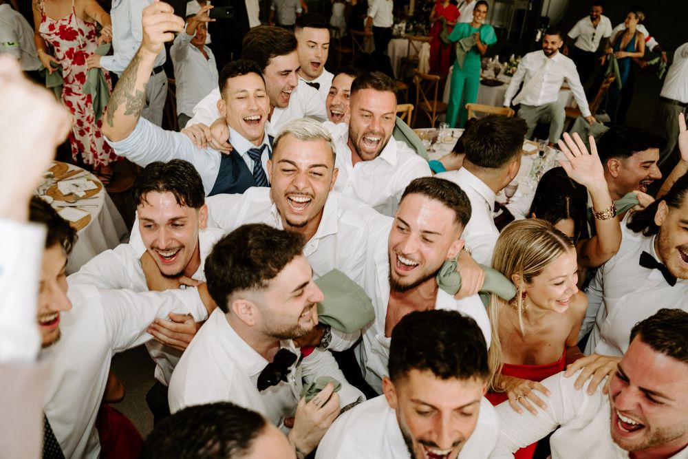 Excited wedding guests huddle together laughing and celebrating on the dance floor at reception.