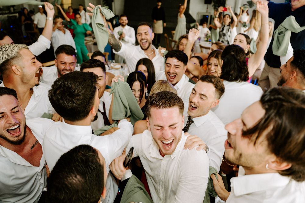 Joyful wedding guests celebrating on the dance floor, smiling and raising hands in excitement.
