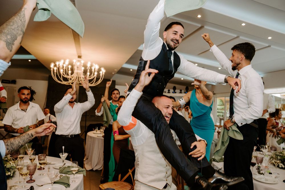 Groomsmen lifting groom in air during lively indoor wedding reception party.
