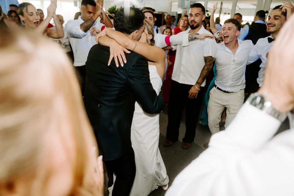 Bride and groom sharing an embrace on the dance floor surrounded by cheering wedding guests.
