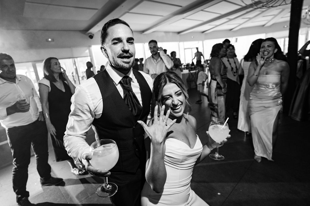 Black and white photo of a joyful bride and groom dancing at their wedding reception, bride showing off her ring.