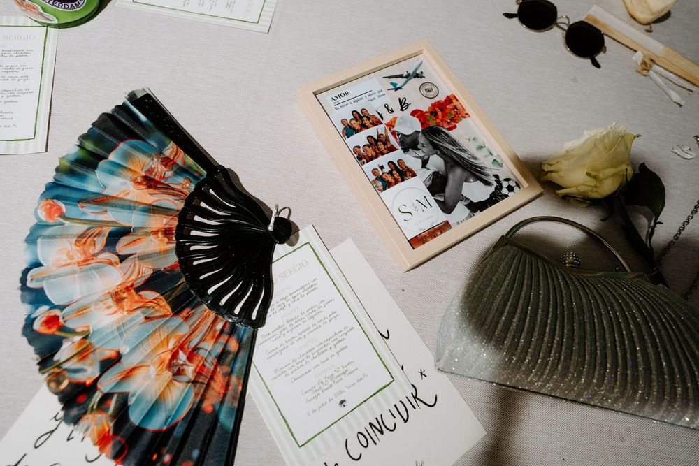 Colorful hand fan, sunglasses, floral arrangement, and elegant stationery displayed on a light gray table.