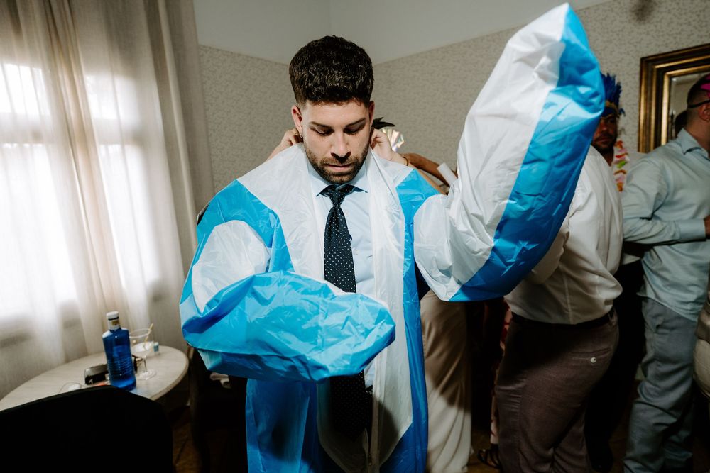 Groom unwrapping blue and white gift bags while getting ready indoors before his wedding ceremony.