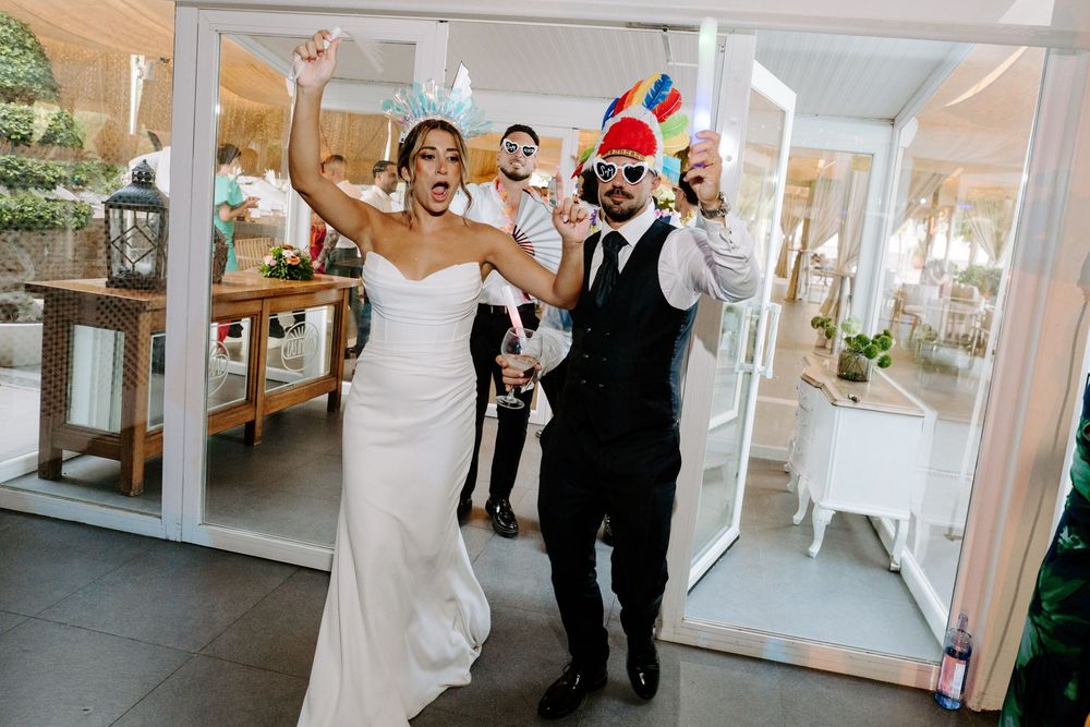 Joyful bride and groom celebrating their wedding entrance, with guests cheering in a bright, elegant venue.