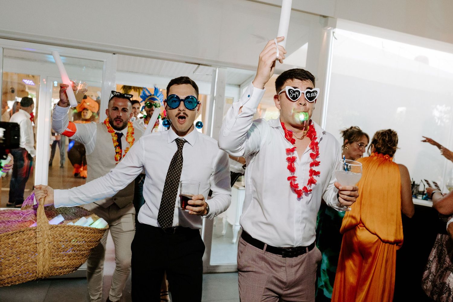 Men in novelty sunglasses and party accessories celebrate at a festive indoor wedding reception party.