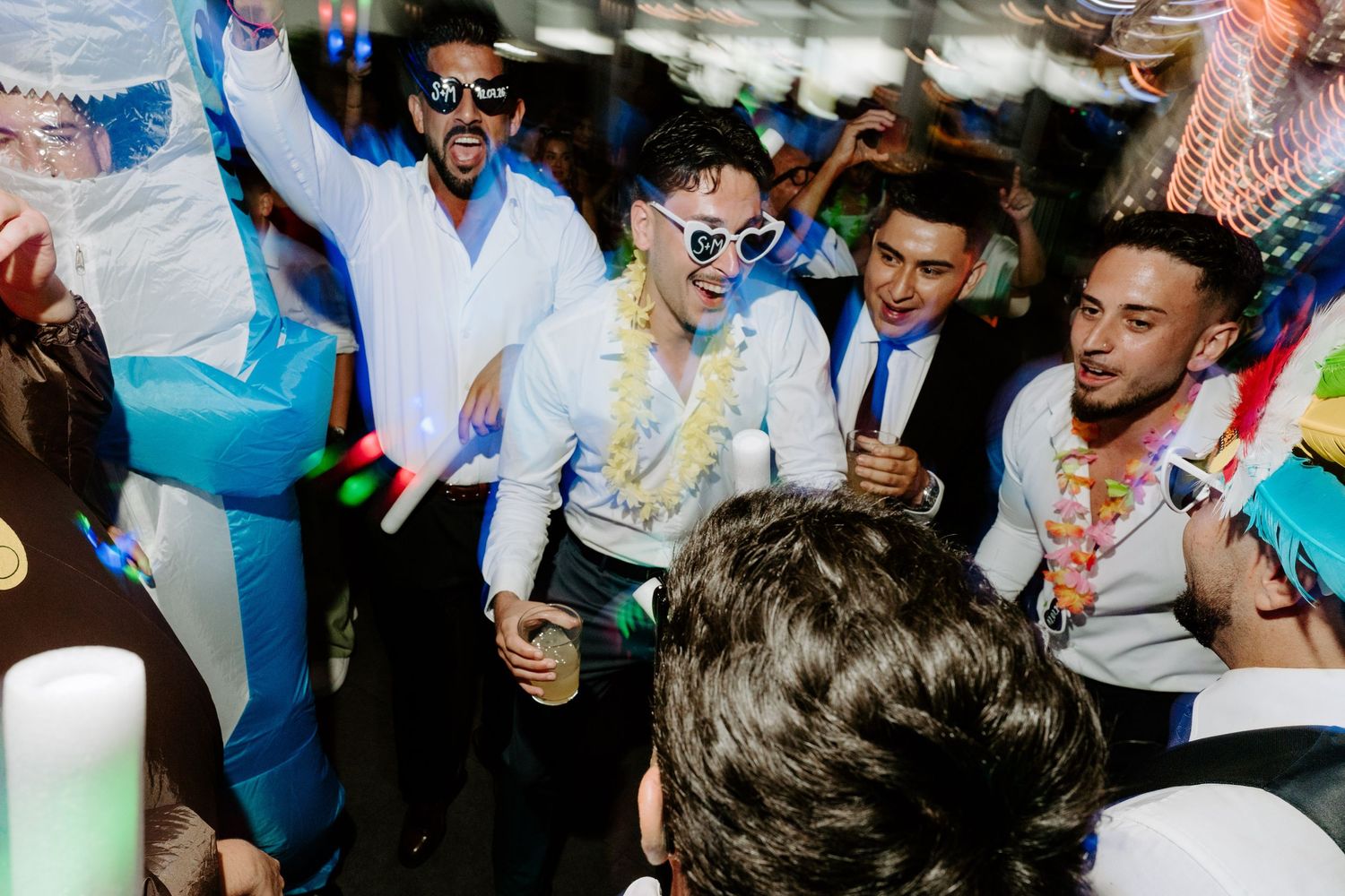 Group of young men dancing and celebrating at a lively party under a tent with colorful decorations.