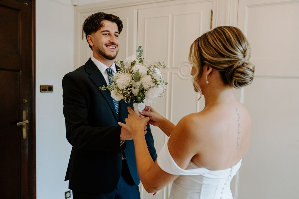 Smiling groom in navy suit receives white bouquet from bride during wedding first look.