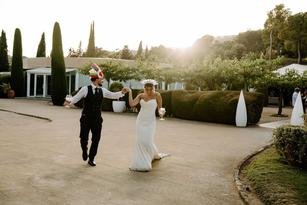 Bride and groom dancing joyfully in a sunlit courtyard surrounded by lush greenery at a wedding venue.
