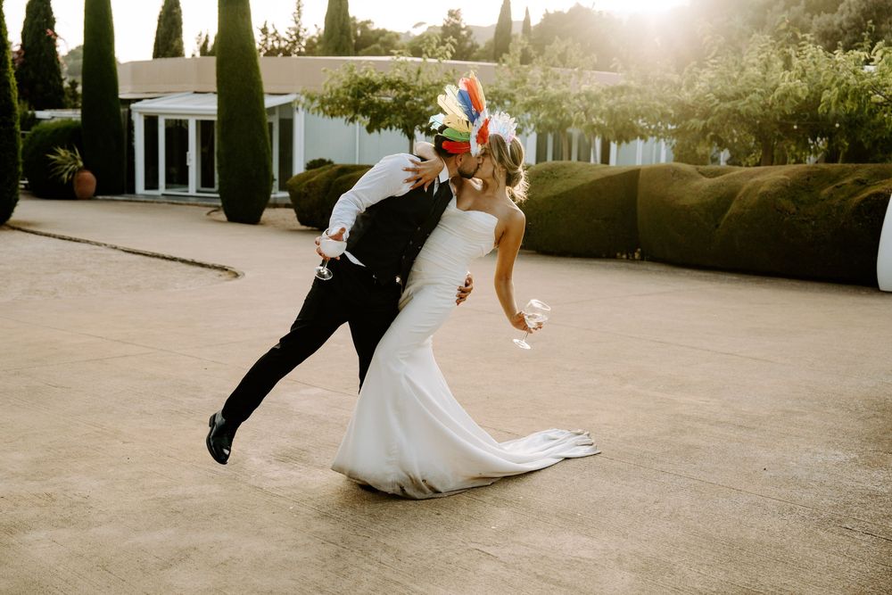 Groom dips bride in white gown during romantic outdoor wedding dance at sunset.