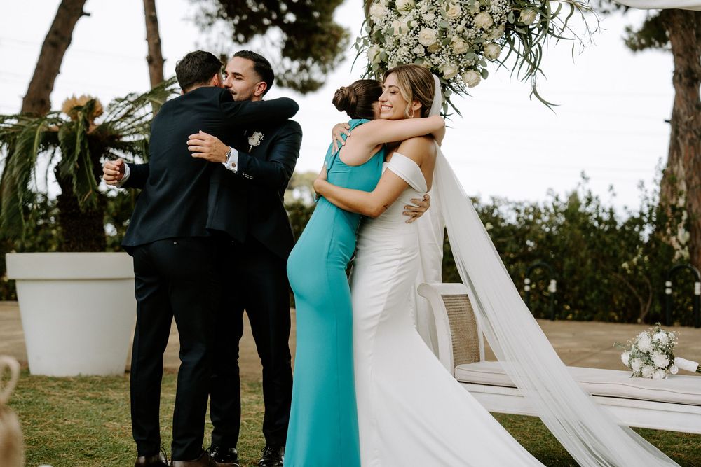 Bride and groom embracing family members after outdoor wedding ceremony near floral arch.