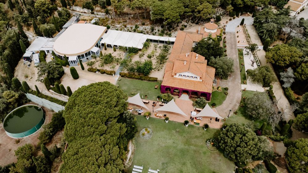 Aerial view of a luxury villa estate with lush gardens, pool, and terracotta roof surrounded by pine trees.