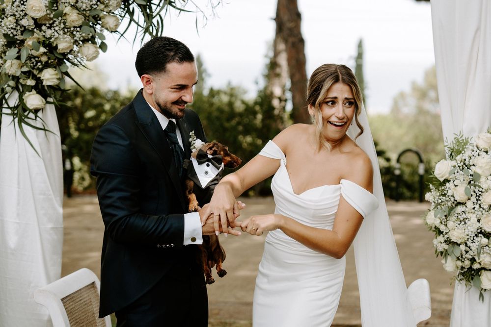 Joyful bride and groom laugh together at outdoor wedding altar adorned with white flowers.