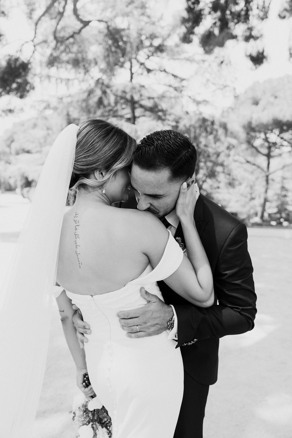 Black and white photo of groom kissing bride in strapless gown with spine tattoo after wedding ceremony.
