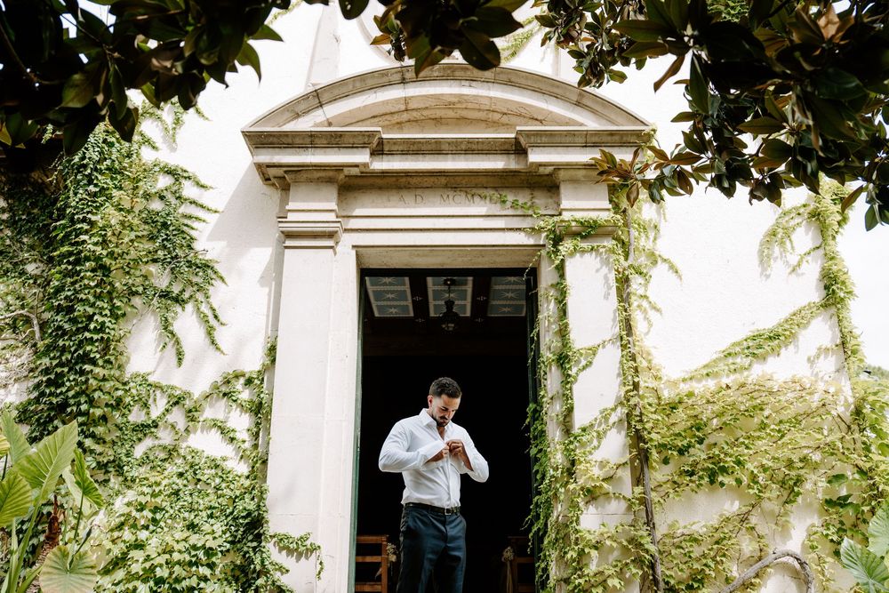 Man adjusting tie outside elegant white building entrance covered in lush green ivy vines.