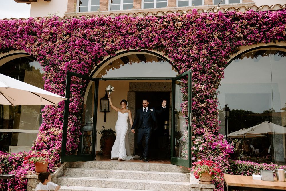 Bride and groom celebrate under a stunning bougainvillea-covered arch at a romantic wedding venue.