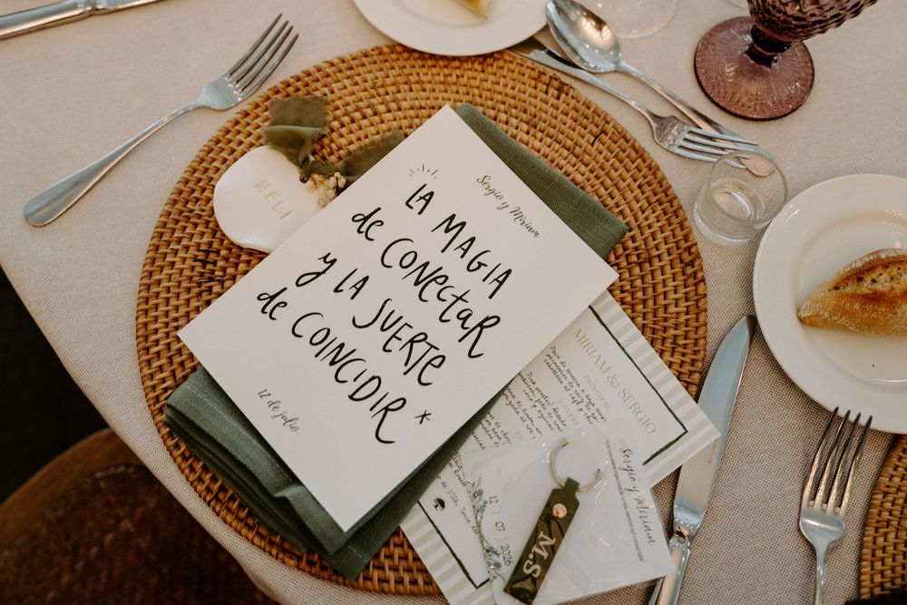 Elegant wedding table setting with calligraphy menu card on woven placemat with green napkin and silverware.